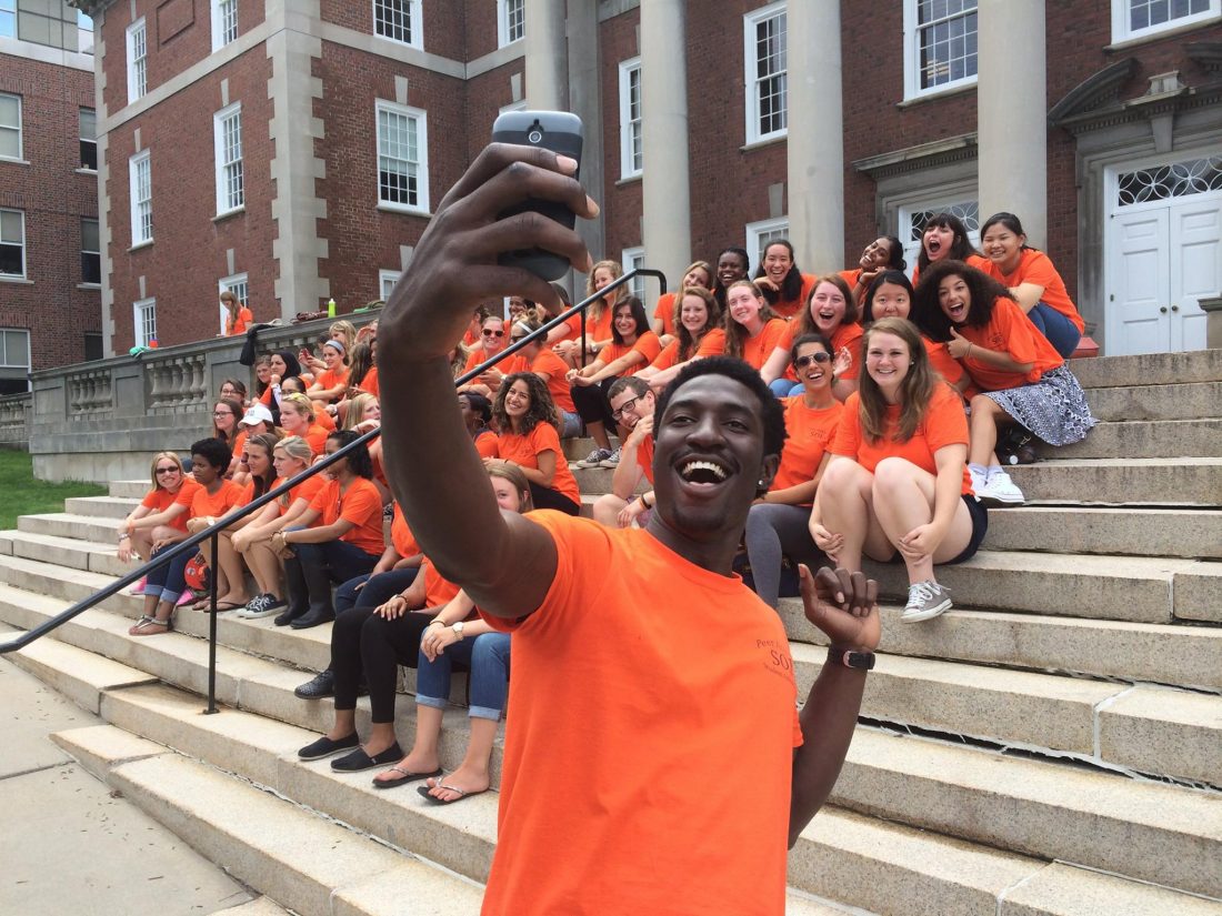 a student in a peer advisor shirt takes a group selfie in front of fellow peer advisors