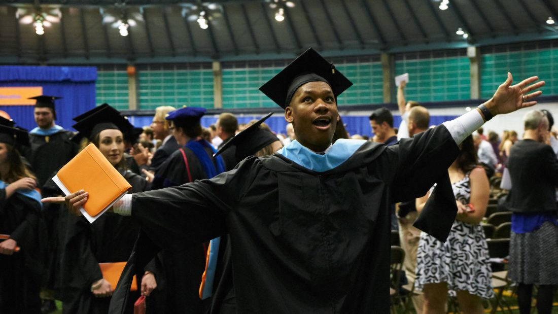 student in cap and gown cheering at graduation