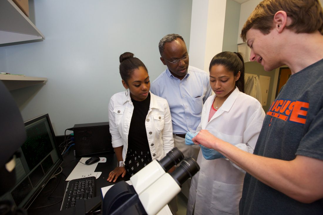 Scientists discuss data in front of a microscope.