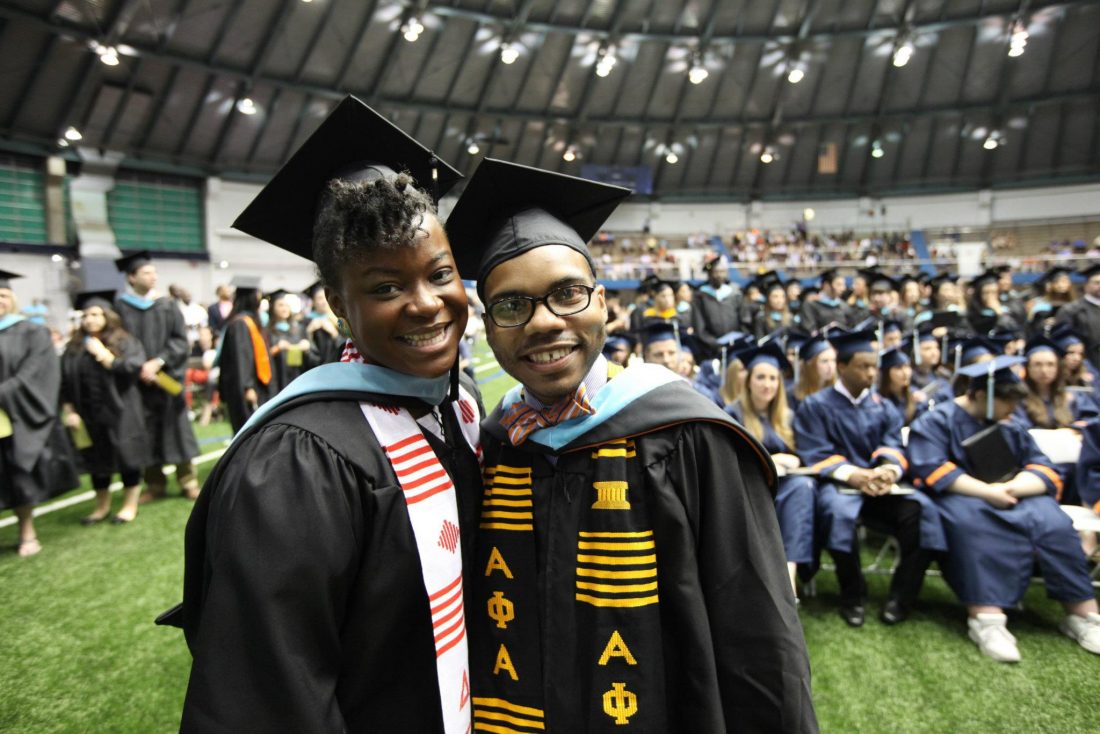 two master's graduates pose for the camera and smile inside manley field house