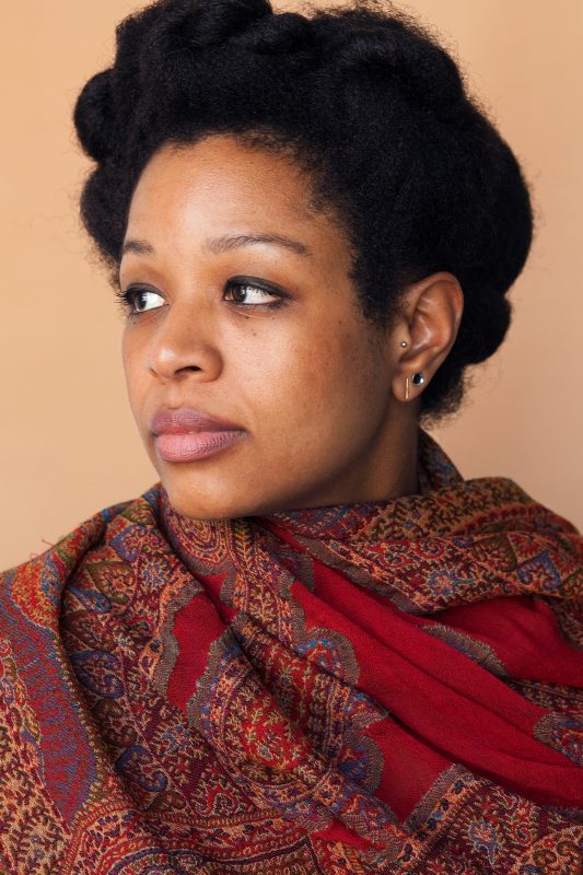 Black woman in profile with short dark hair and a bold red and brown scarf wrapped around her neck