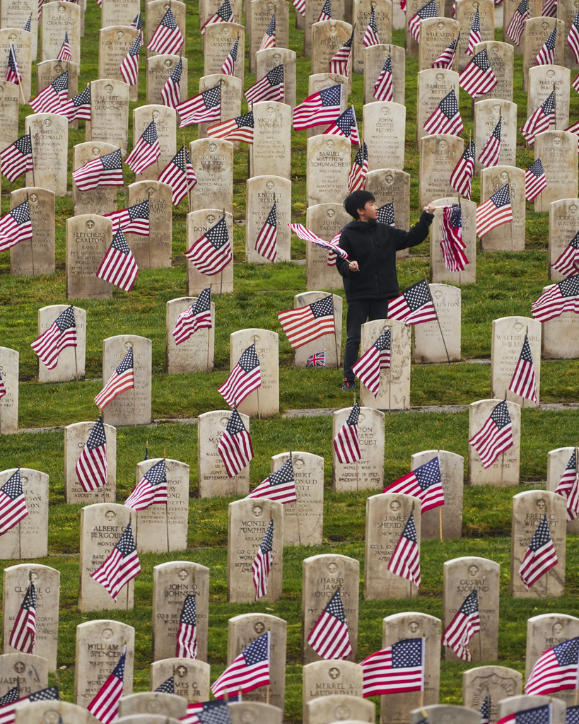 boy standing in cemetery with flags in front of grave