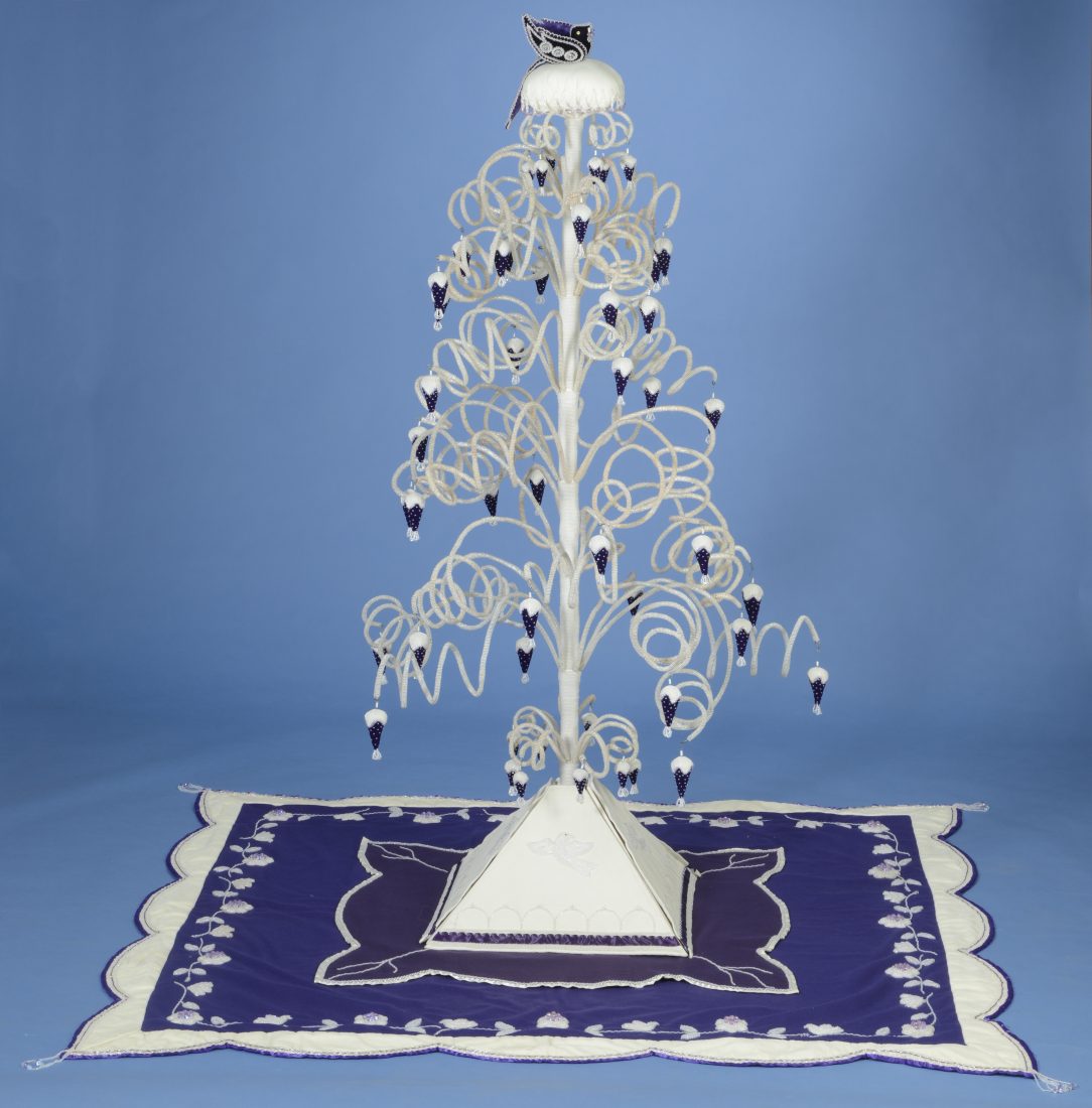 white plastic tree with dropping leaves and a white base, placed on a blue rug with white detail and border