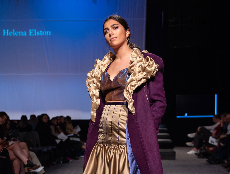 A model poses on stage in a student design during a fashion show.
