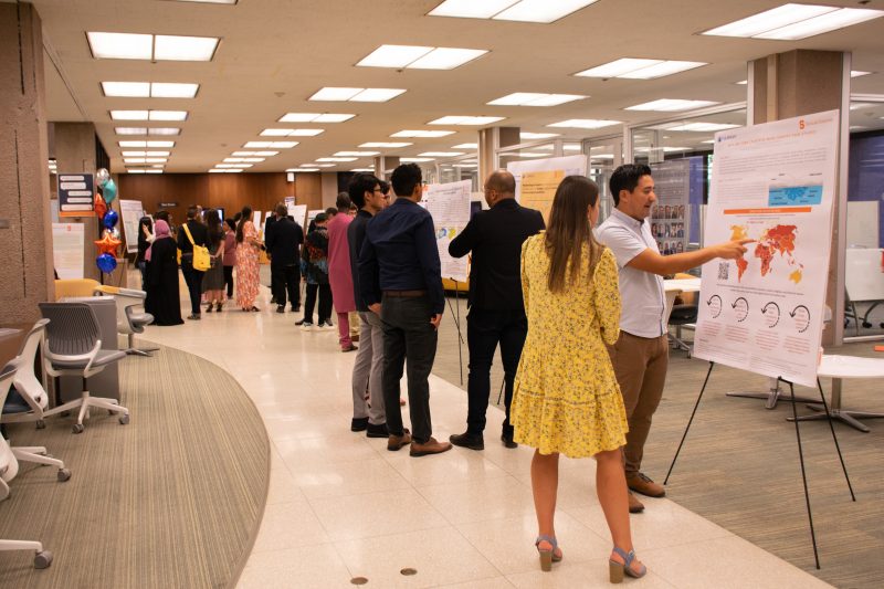 students and visitors standing near posters set up around room