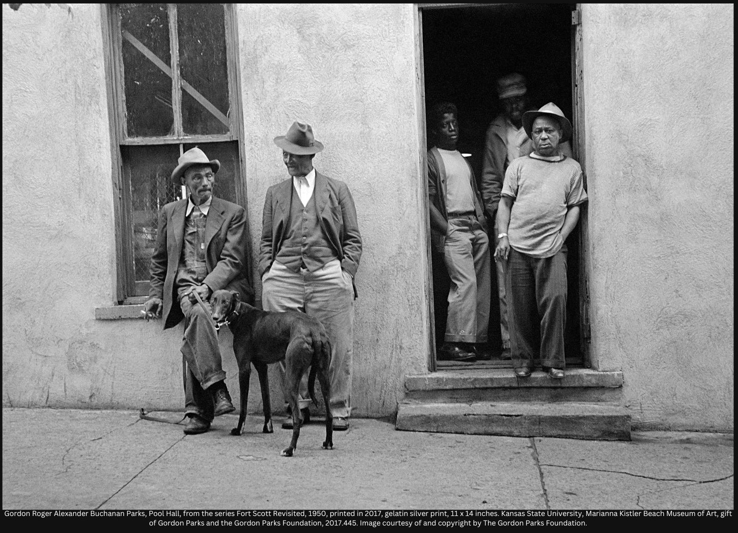 Black and White photo of a number of people standing outside in front of a building, one holding a dog