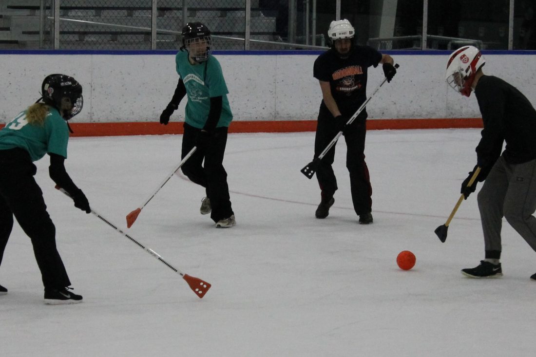 Two broomball players attempt to advance the ball past two defenders.