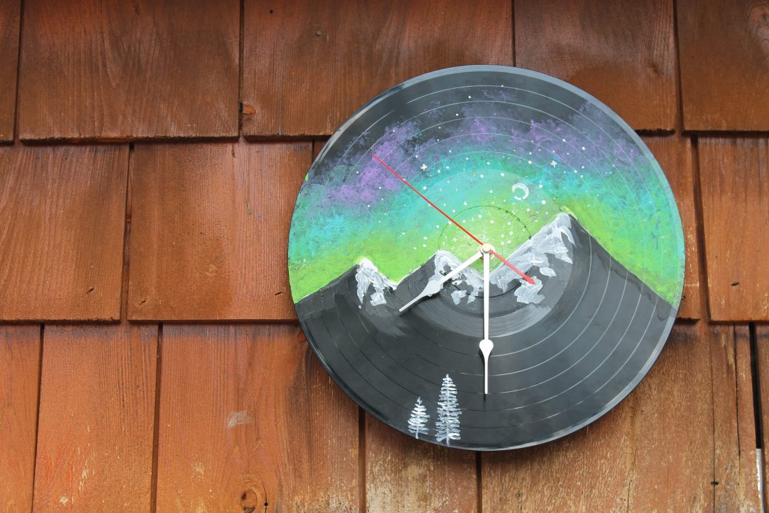 A vinyl record clock with a mountain painted on it. 