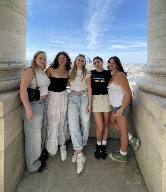 5 people standing between two pillars with a blue sky in the background.