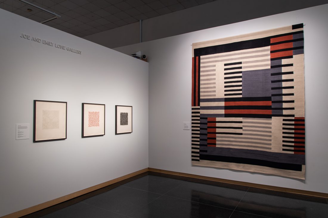 Museum interior with artwork on the walls to the left and a hanging textile to the right