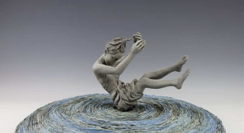 A sculpture of a person sitting on a wavelike surface with their arms and legs in the air