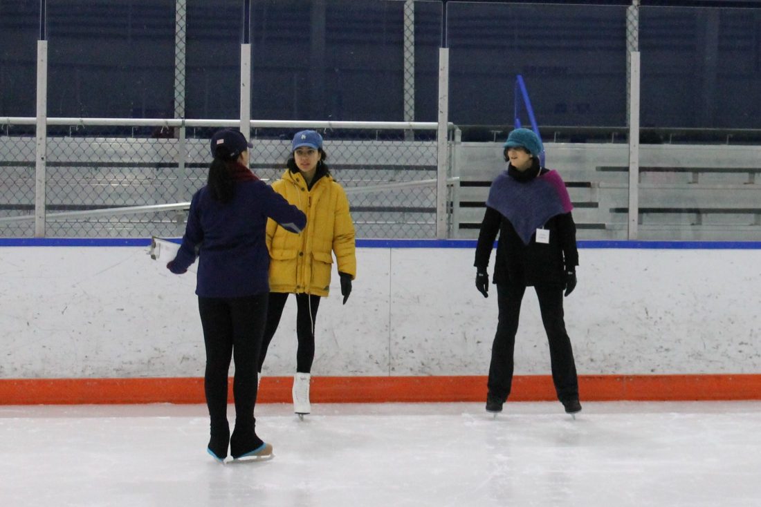 Two students stand on the ice in Tennity Ice Pavilion as an instructor talks to them.
