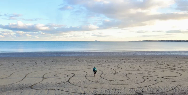A person walks on a large beach with circular patterns in the sand
