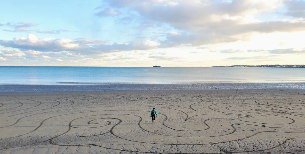 A person walks on a large beach with circular patterns in the sand