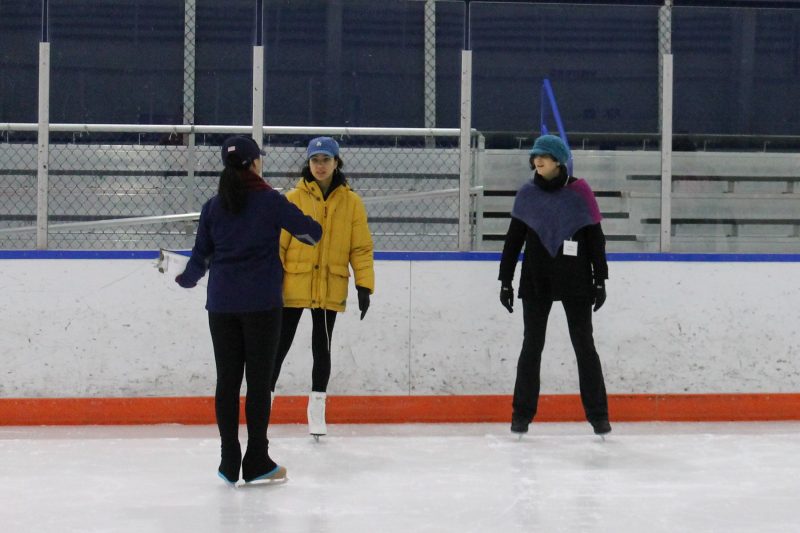 A skating instructor teaches ice skating to two students.