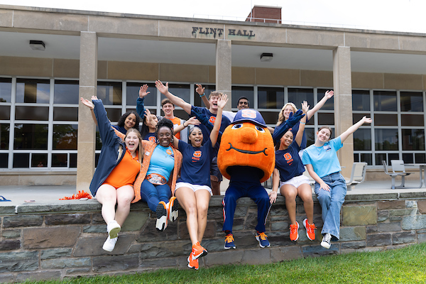 A group of students and mascot in front of a residence hall.