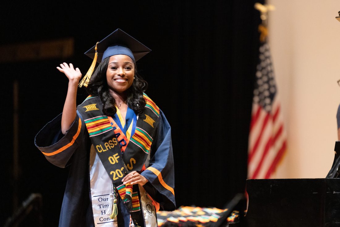 Student walks across the stage and waves at Itanwa Orinwa 2022 ceremony