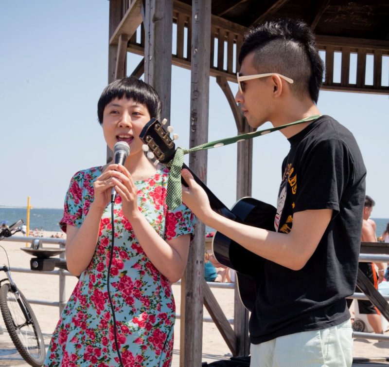 artist Pixy Liao sings into microphone while partner Takahiro Morooka strums guitar