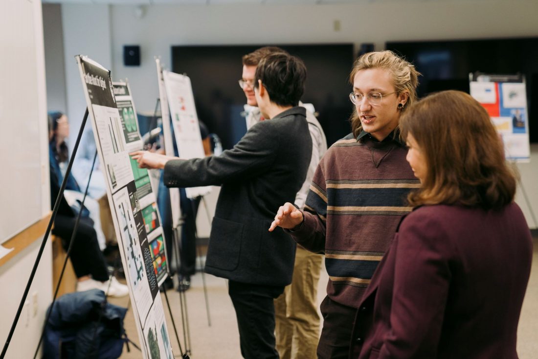 Students explaining their posters to faculty