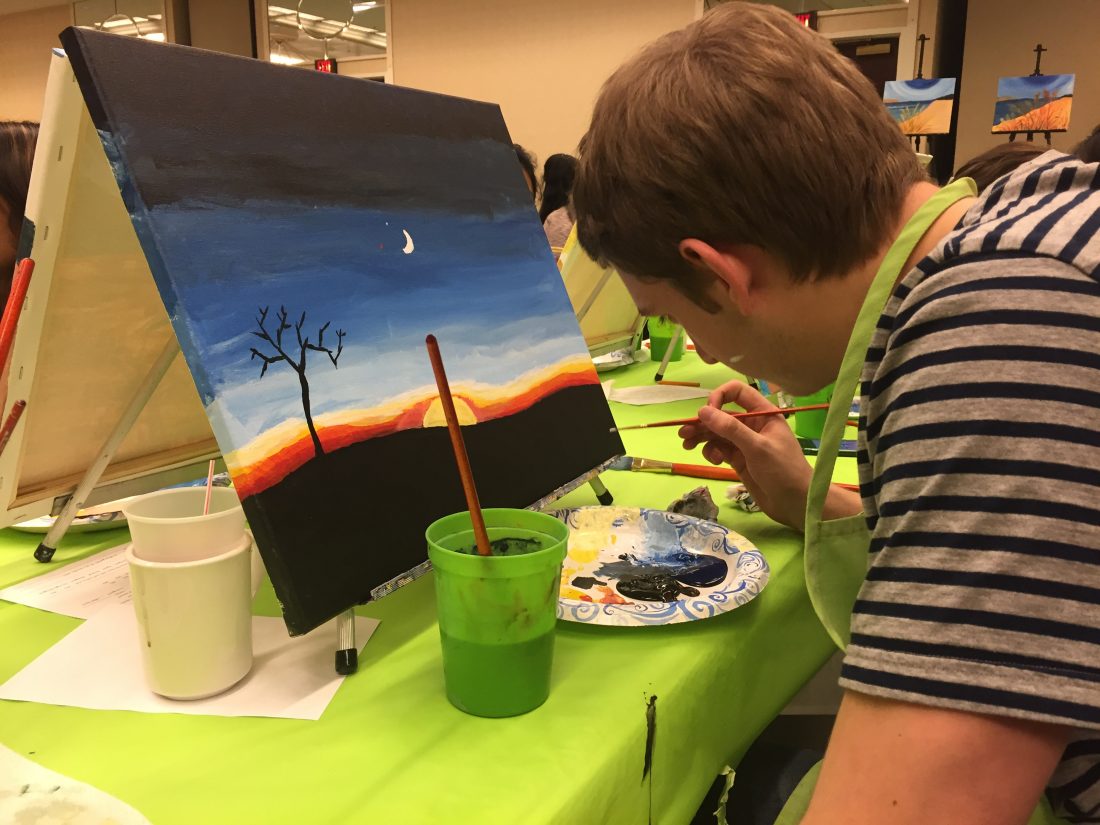 A student paints a desert sunset at Orange After Dark Paint Night