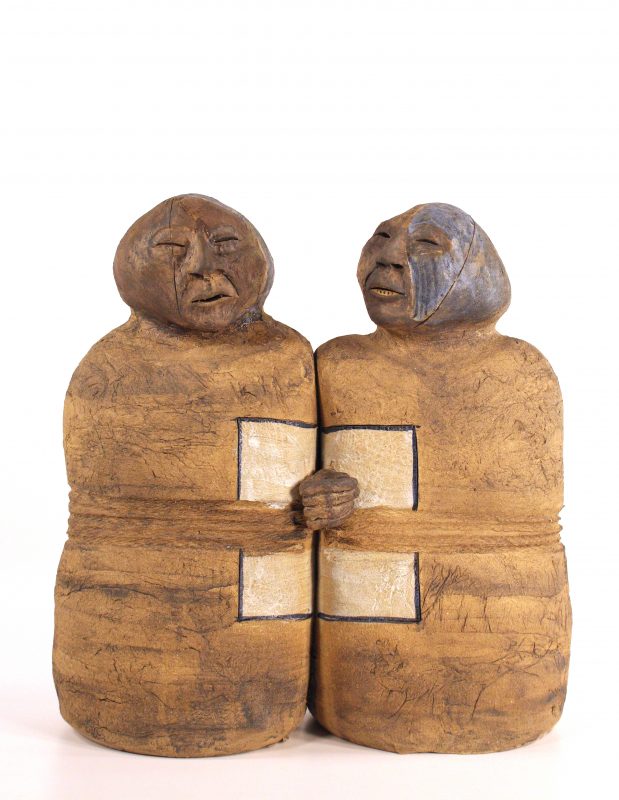 ceramic sculpture of two abstract figures joined at the mid section, holding hands, in tan colors