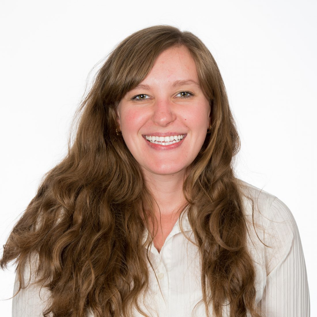 A close-up color photo of Dr. Alesia Prakapenka, smiling with full-teeth and long, wavy brown hair against a solid background. 