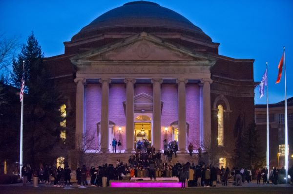 Syracuse University Hendricks Chapel illuminated purple and with many people out front for the Take Back The Night event.
