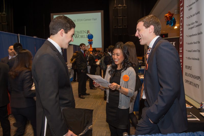 Well-dressed students laugh with a recruiter at the spring career fair.