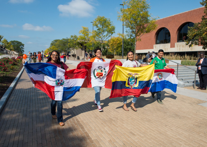 A group of Latinx students walk down Einhorn Family Walk with various flags of their countries.