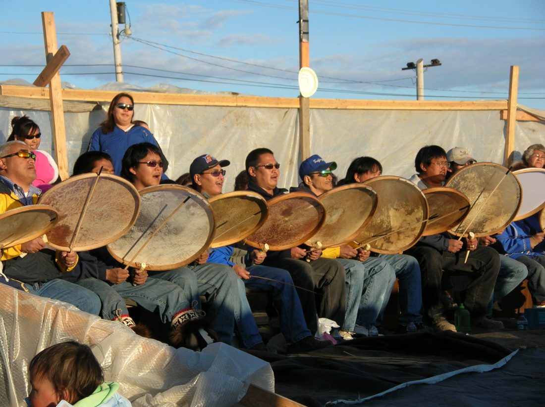 Indigenous people sitting in a line playing traditional drums