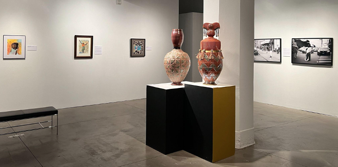 A gallery with illustrations and photographs hung on the wall and ceramic vessels on pedestals.