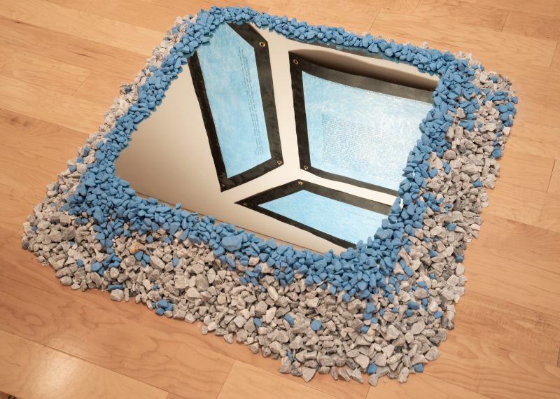 Mirror placed on wooden floor, on top of a pile of white and blue rocks