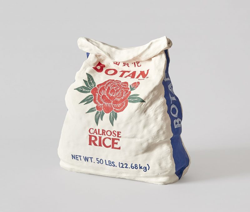 A sculpted rice bag in the center of the light gray background, with a red rose on the front of the cream colored bag