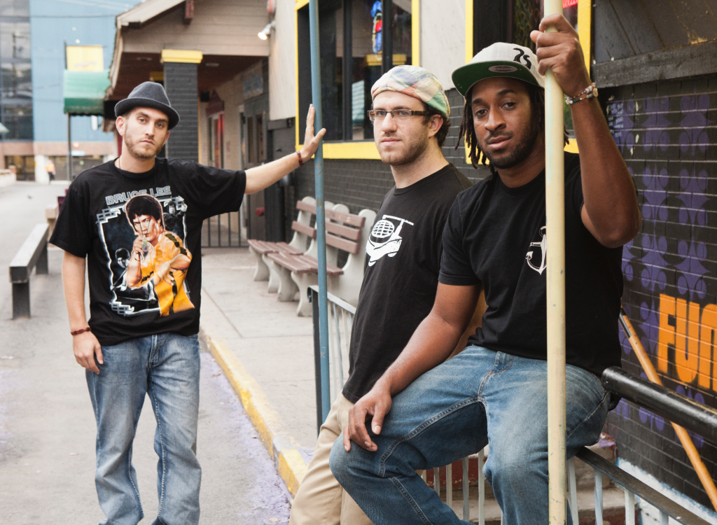 Three members of band sophistafunk pose together in an alleyway