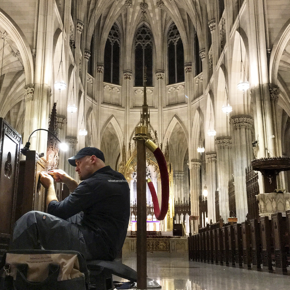 A man carves a wooden pew in a cathedral