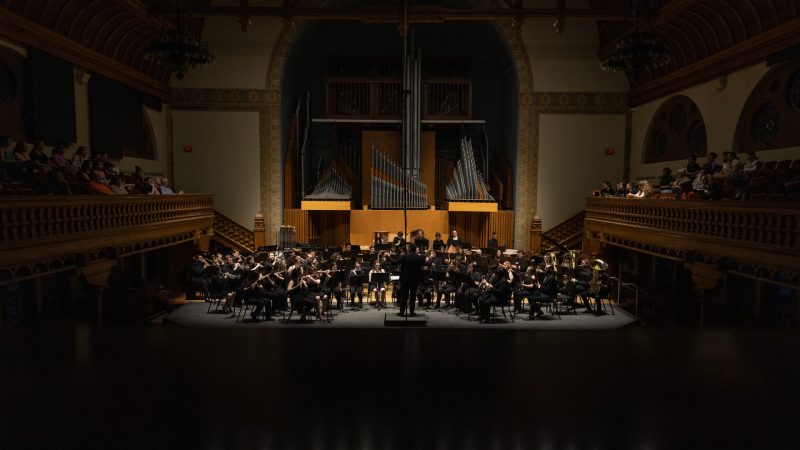 The Syracuse University Wind Ensemble performs on stage.