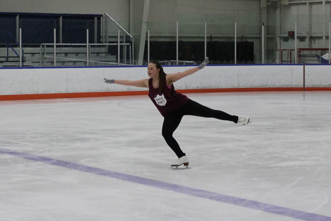 A figure skater wearing a sleeveless shirt lands a jump on one skate with her arms outstretched.