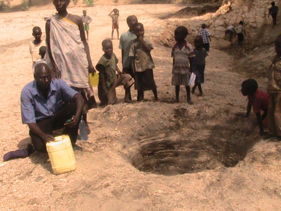 People in an unknown African location line up to draw water from a pit.