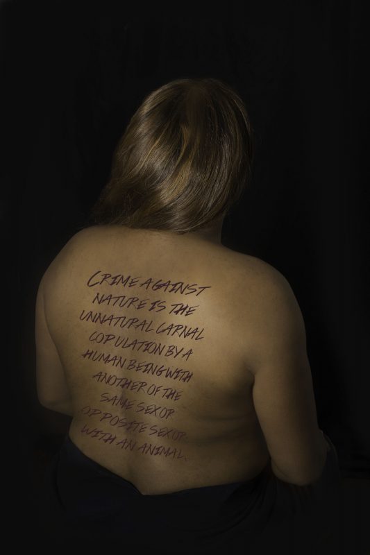 artistic photograph of a black woman shirtless from teh back, wiht text written over her back.