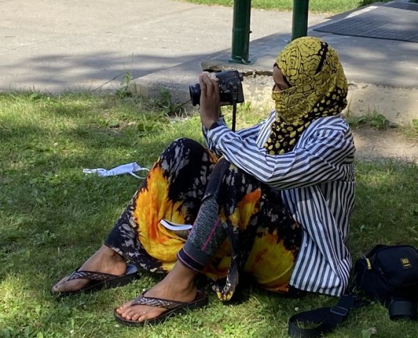 woman seated on grass looking through a camera viewfinder