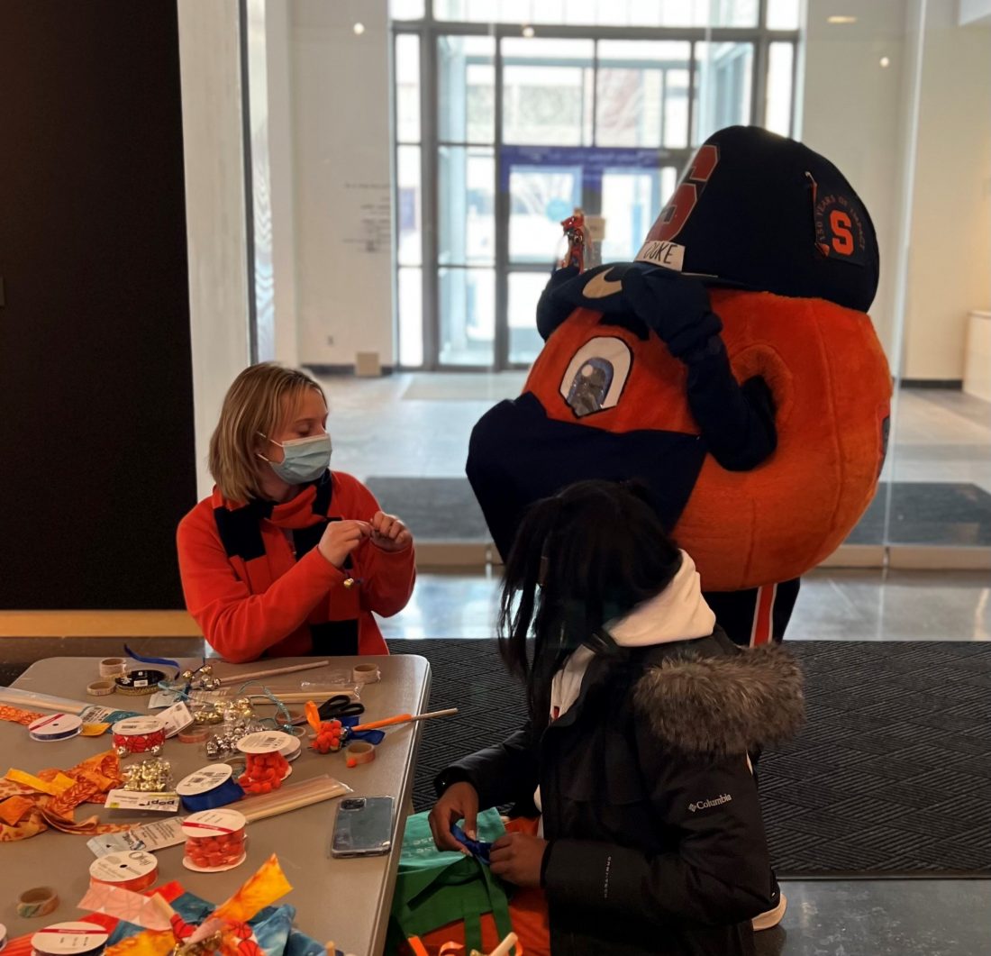 Otto the orange mascot making crafts wiht two females in the museum