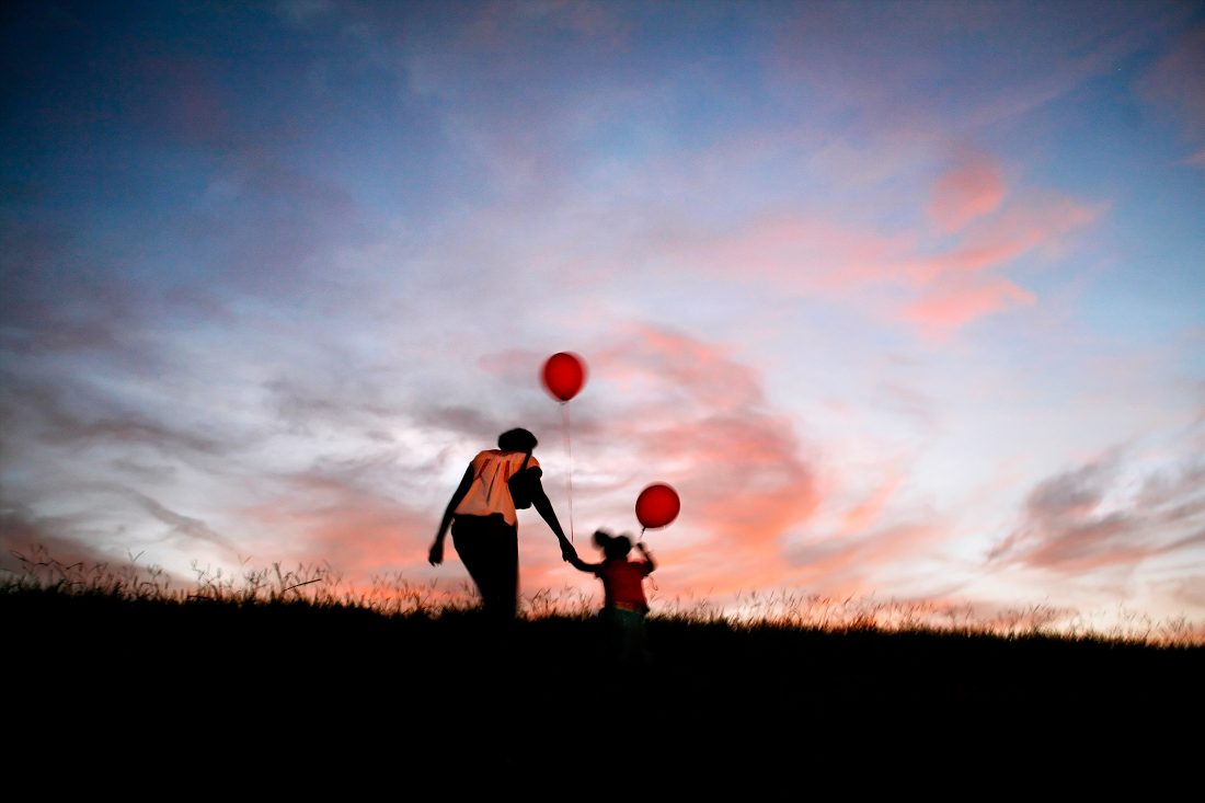 A mother and daughter walk in a field with balloons.