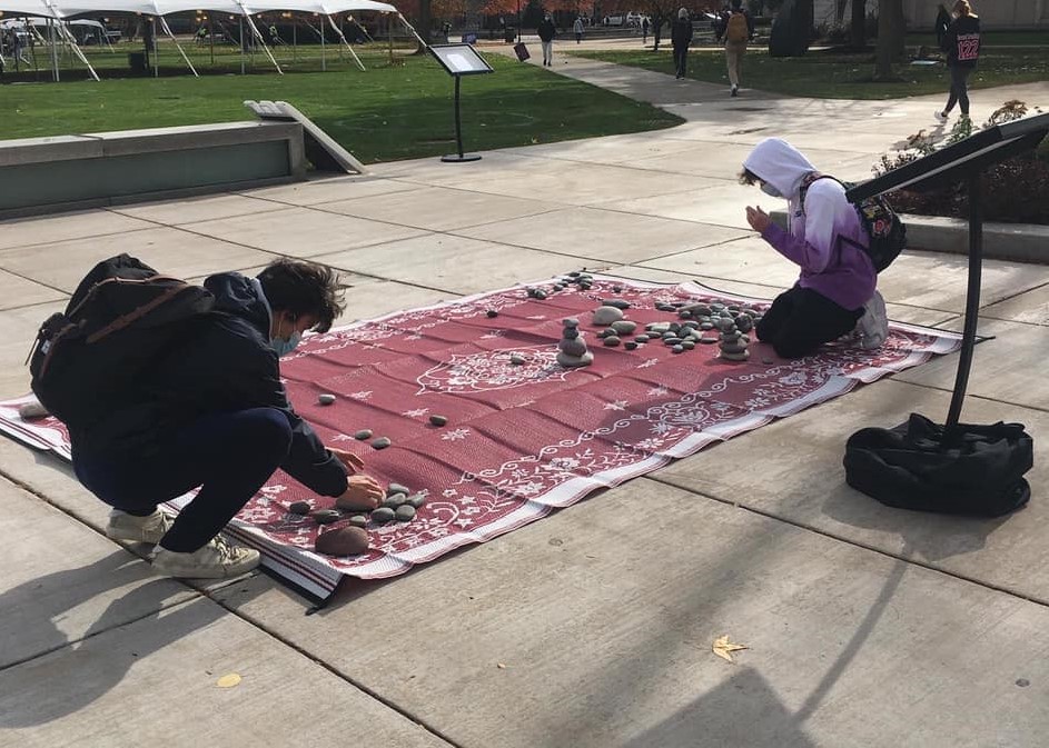 Students kneeling on rug stacking rocks outside