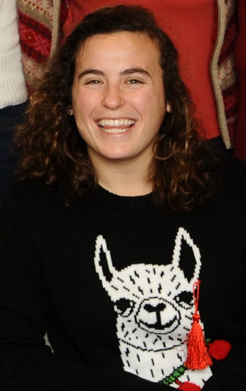 A close-up, color photo of Sarah Weiss smiling for the camera. She wears a black sweater with a white llama printed on it. 