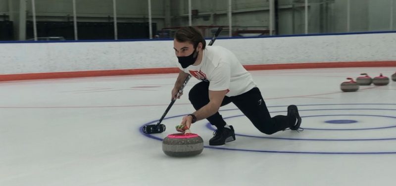 A curler slides in a crouch with a curling stone.