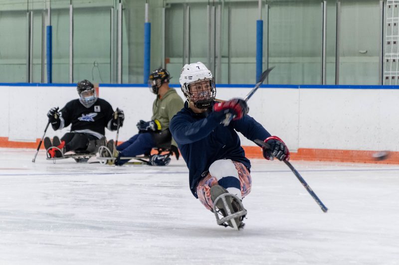 A hockey player in an adaptive sled shoots the puck.