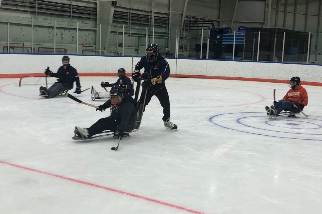 A hockey player in an adaptive sled controls the puck.