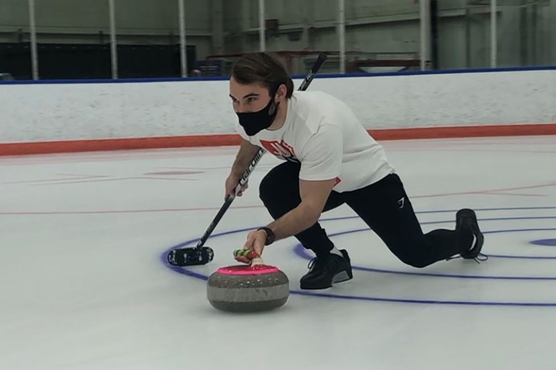 A curler in a crouched position slides a curling stone along the ice.