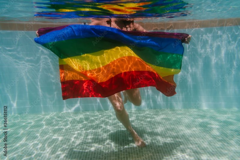 A woman swimming holding an LGBTQ flag underwater