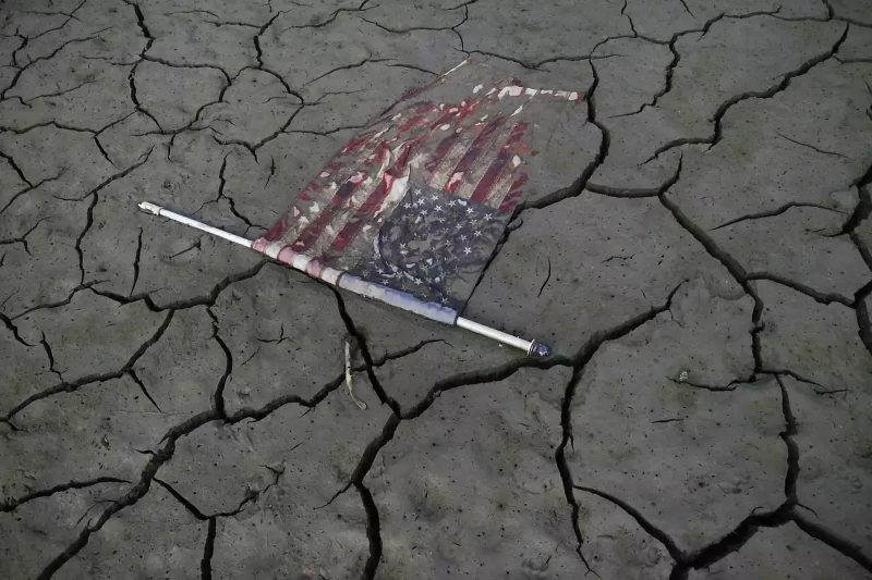 A muddy American flag on the ground of a former lake with dark cracks 